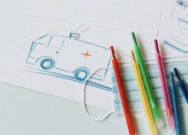 Child's crayon drawing of an ambulance beside a face mask and colored pens